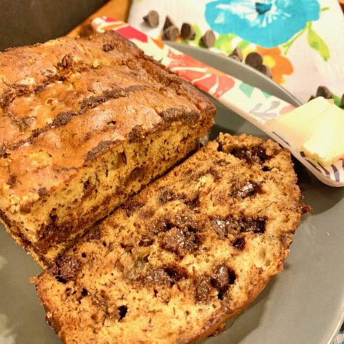 chocolate chip banana bread on gray plate with blue flower fabric napkin surrounded with chocolate chips