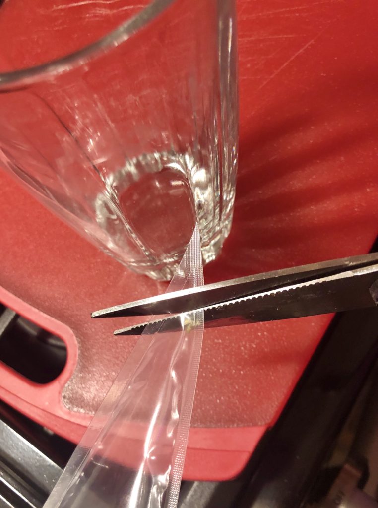 cutting the end off of a pastry bag before draping over a glass to fill with frosting
