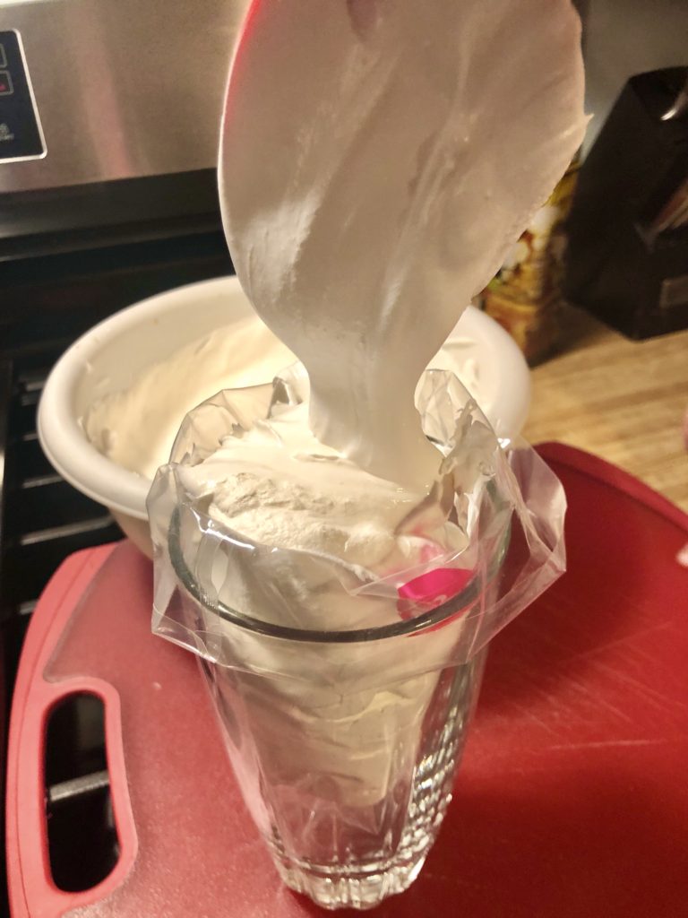 filling pastry bag draped over a clear glass. the bag is being filled with marshmallow frosting