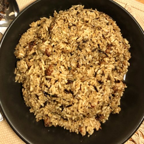 wild rice and sausage stuffing plated in black bowl on tan fabric over wooden cutting board