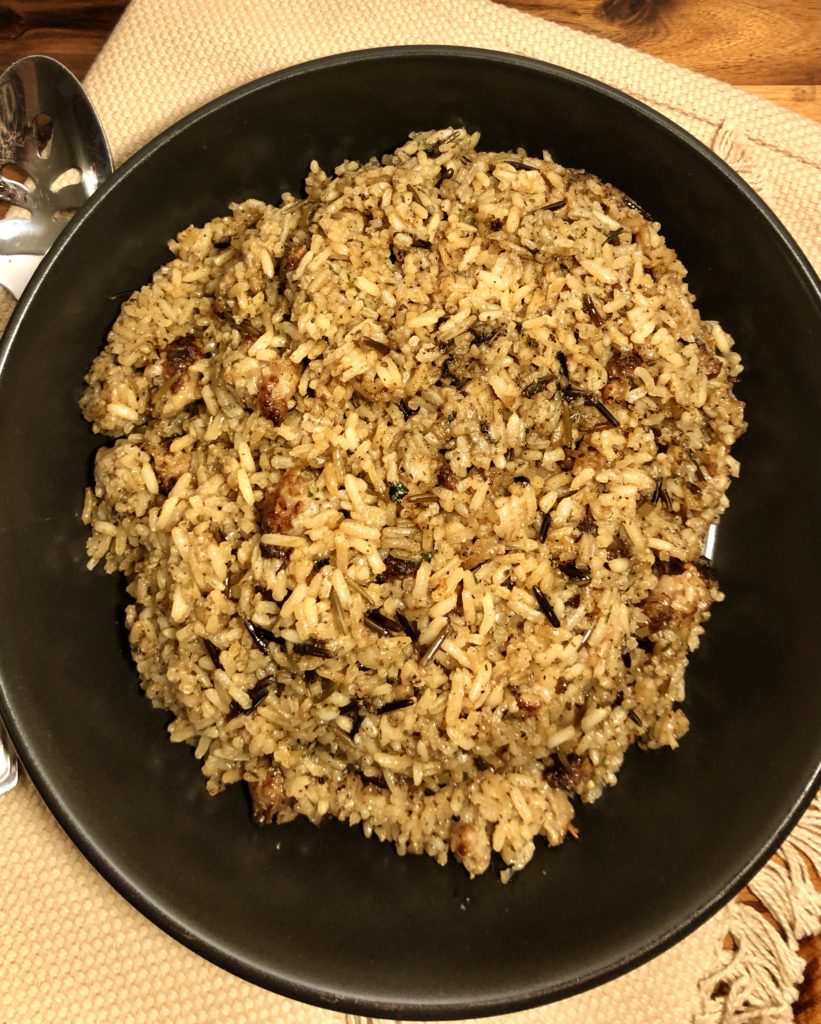 wild rice and sausage stuffing plated in black bowl on tan fabric over wooden cutting board
