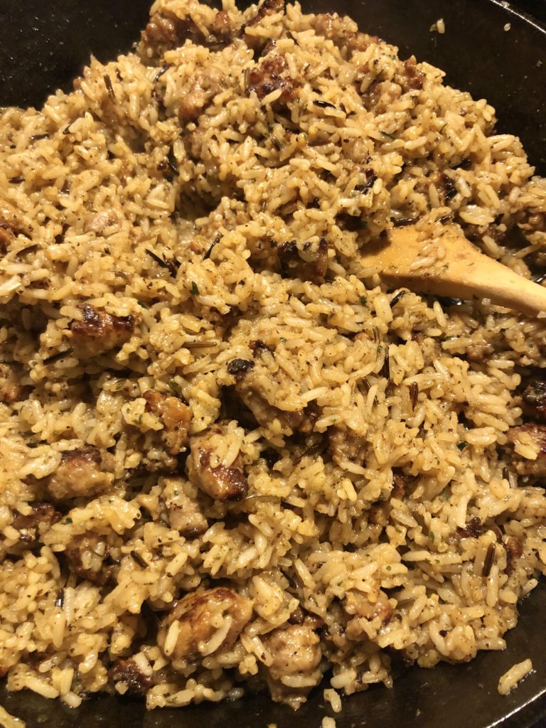 wild rice and sausage stuffing being stirred in skillet with wooden spoon