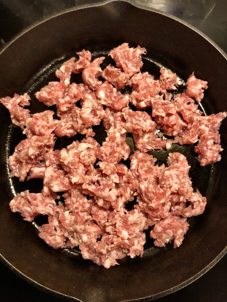 Italian sausage removed from casing and frying in black skillet