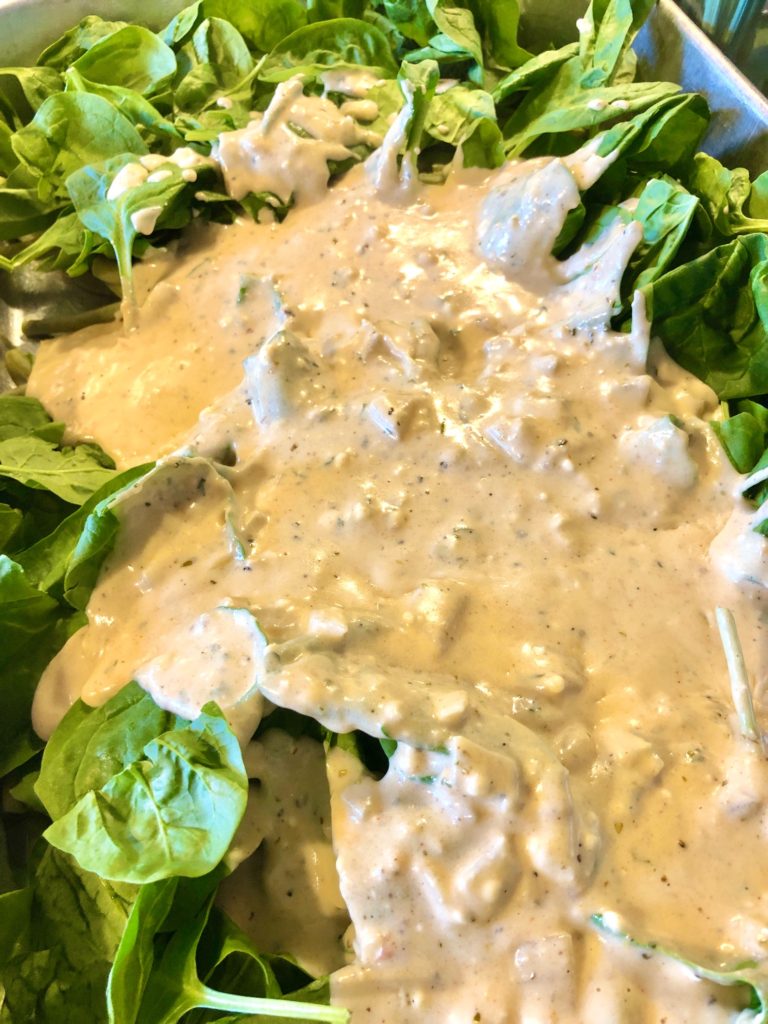 green beans and spinach in baking pan with cream sauce added to top