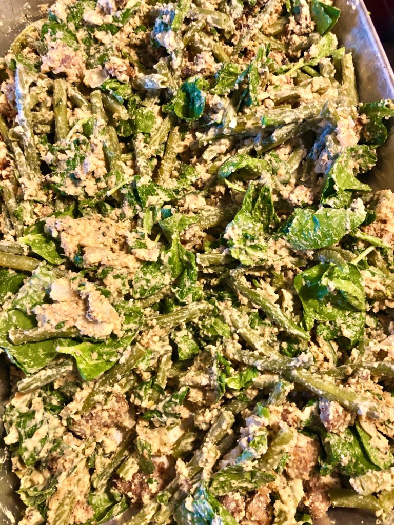 green bean casserole wit spinach, sausage, parmesan bread crumbs and cream sauce in silver baking pan before baking