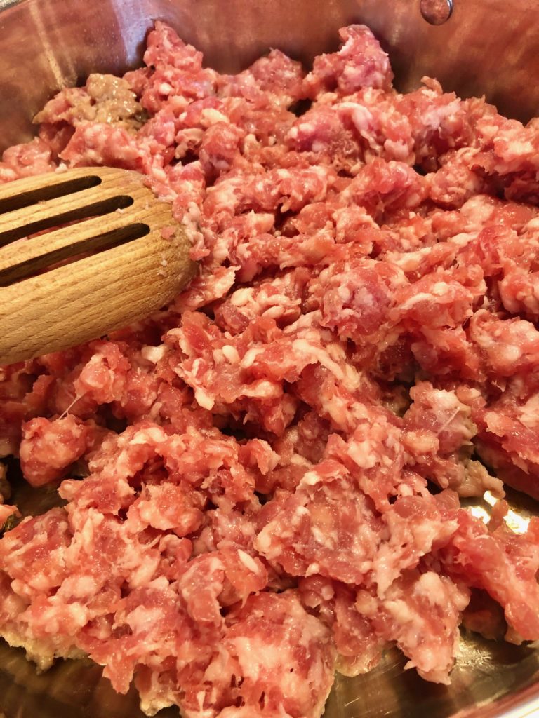 Italian sausage being added to black cast iron skillet and stirred with wooden spoon