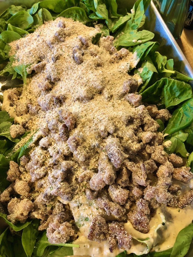 green beans and baby spinach in baking pan covered with cream sauce, sausage and parmesan bread crumb mixture