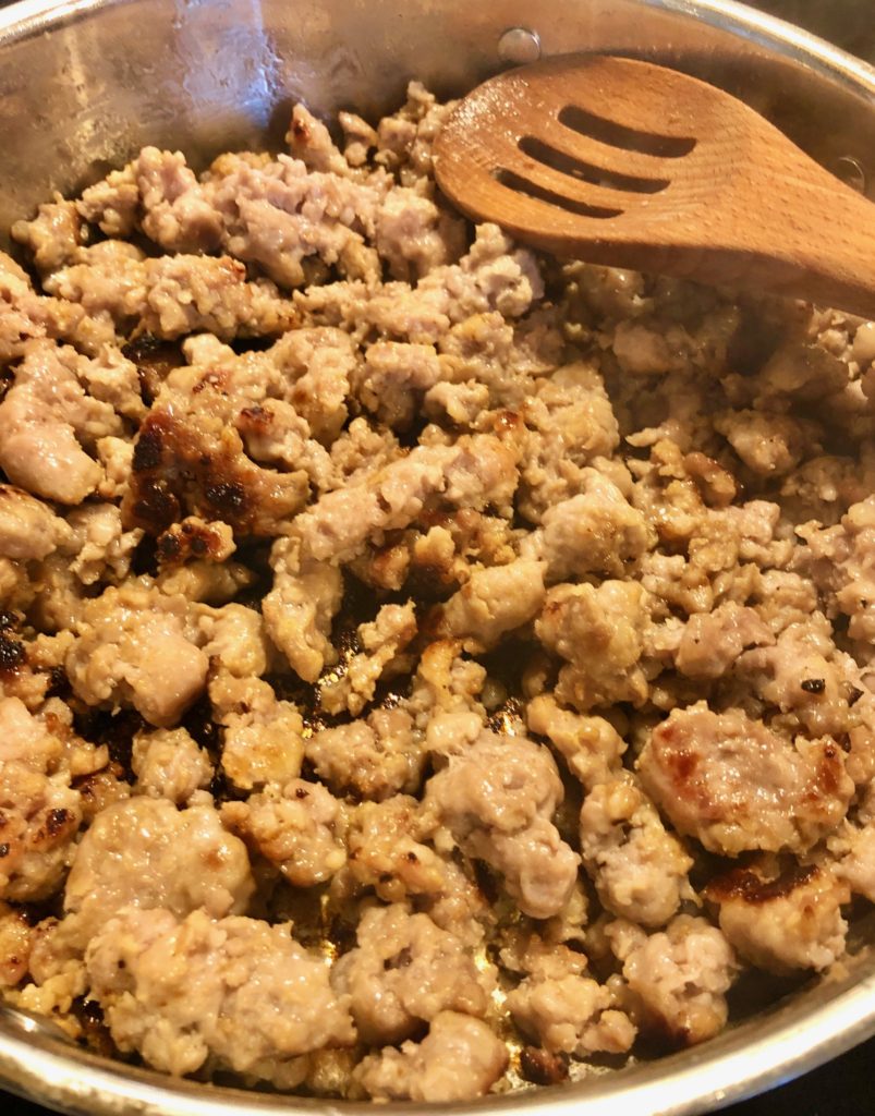 cooked Italian sausage in silver frying pan and being stirred with wooden spoon