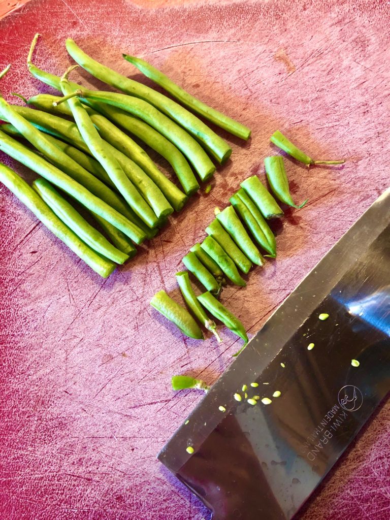 ends being cut off of green beans on red cutting board pictured with butcher knife