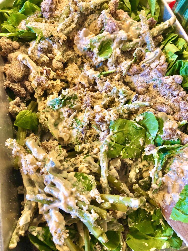 green beans, spinach, sausage breadcrumb mixture and cream sauce being stirred together in silver baking pan