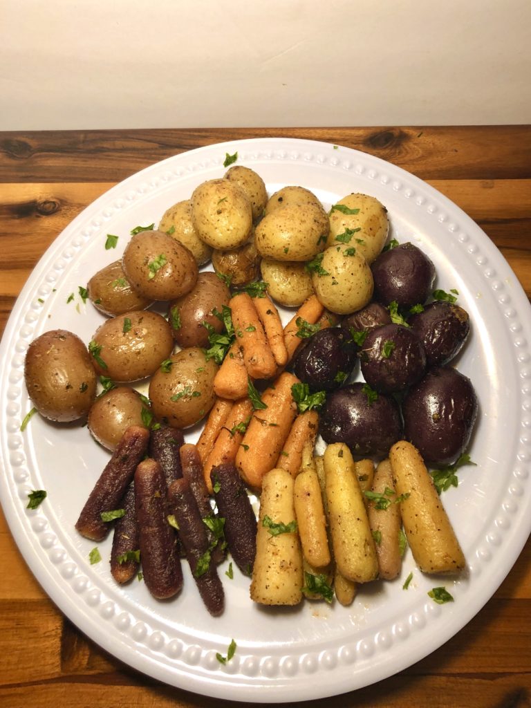 roasted rainbow carrots and baby potatoes plated on white plate against wooden cutting board. fresh cut parsley used as garnish over the top.