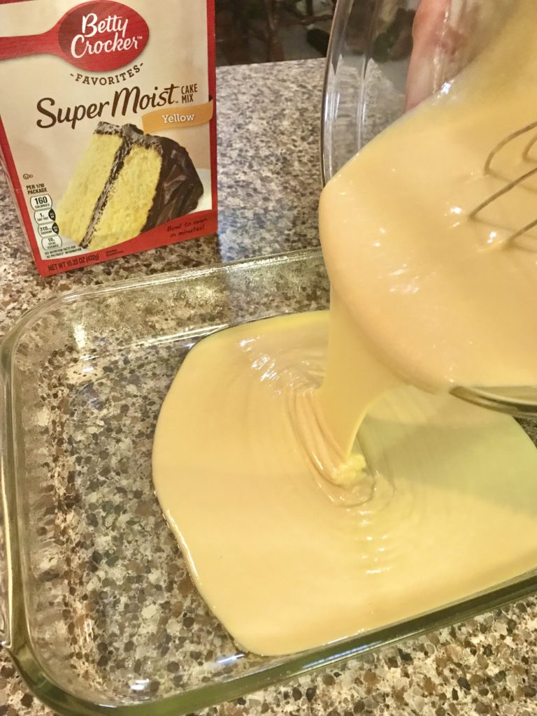 pouring prepared yellow cake mix into glass baking dish with cake mix box in the background