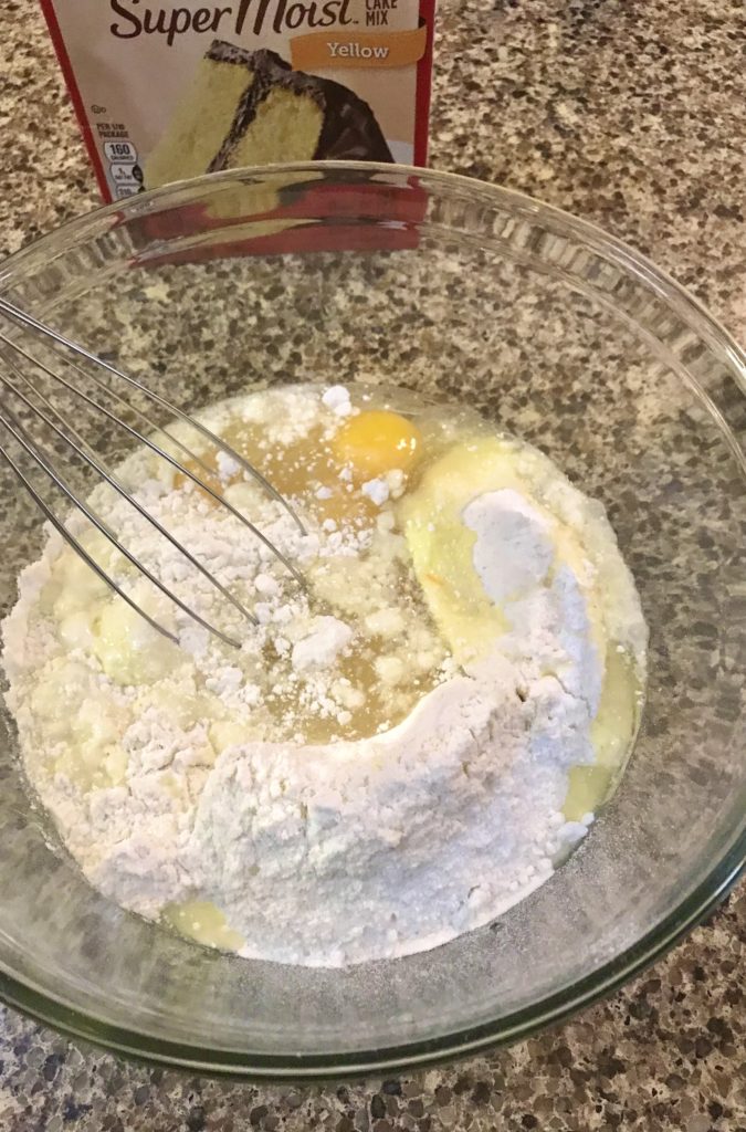 yellow cake mix, egg, water and vegetable oil in glass mixing bowl being whisked