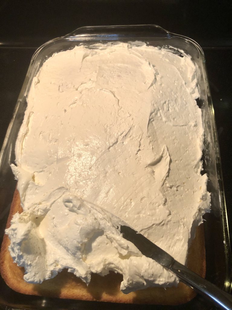 spreading cream cheese and cool whip frosting over the top of prepared yellow cake mix