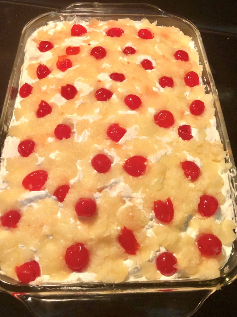 overhead view of yellow better than sex cake with cream cheese and cool whip frosting and covered with crushed pineapples and maraschino cherries