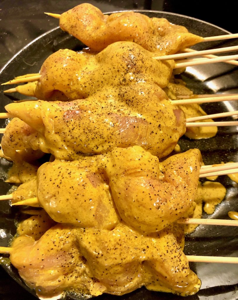 marinated chicken satay skewers on black plate