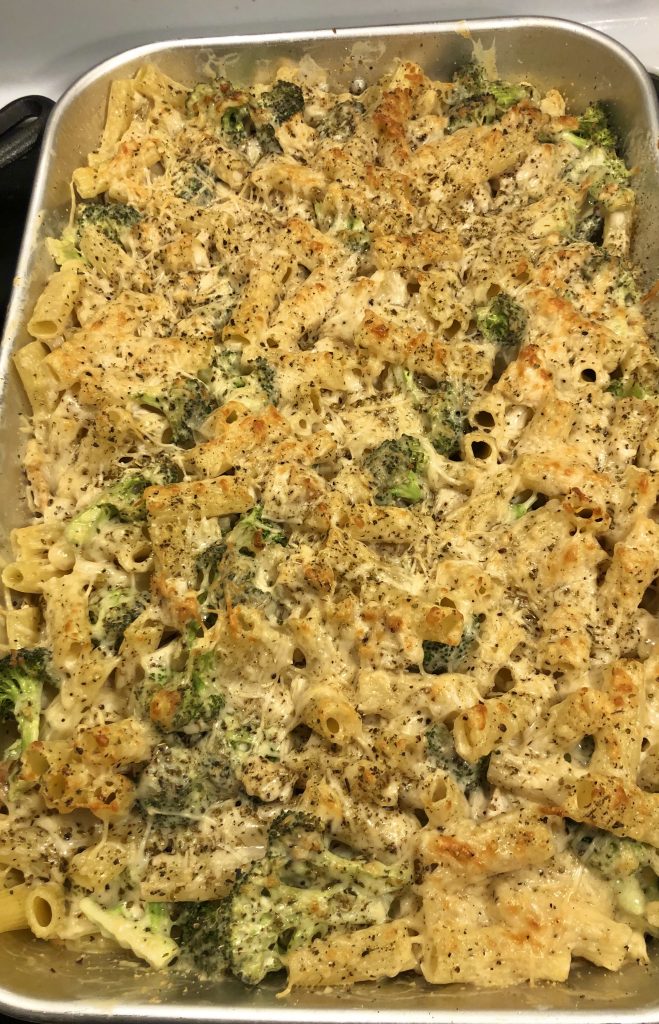 chicken broccoli and ziti with shredded parmesan cheese and herb topping in silver baking dish