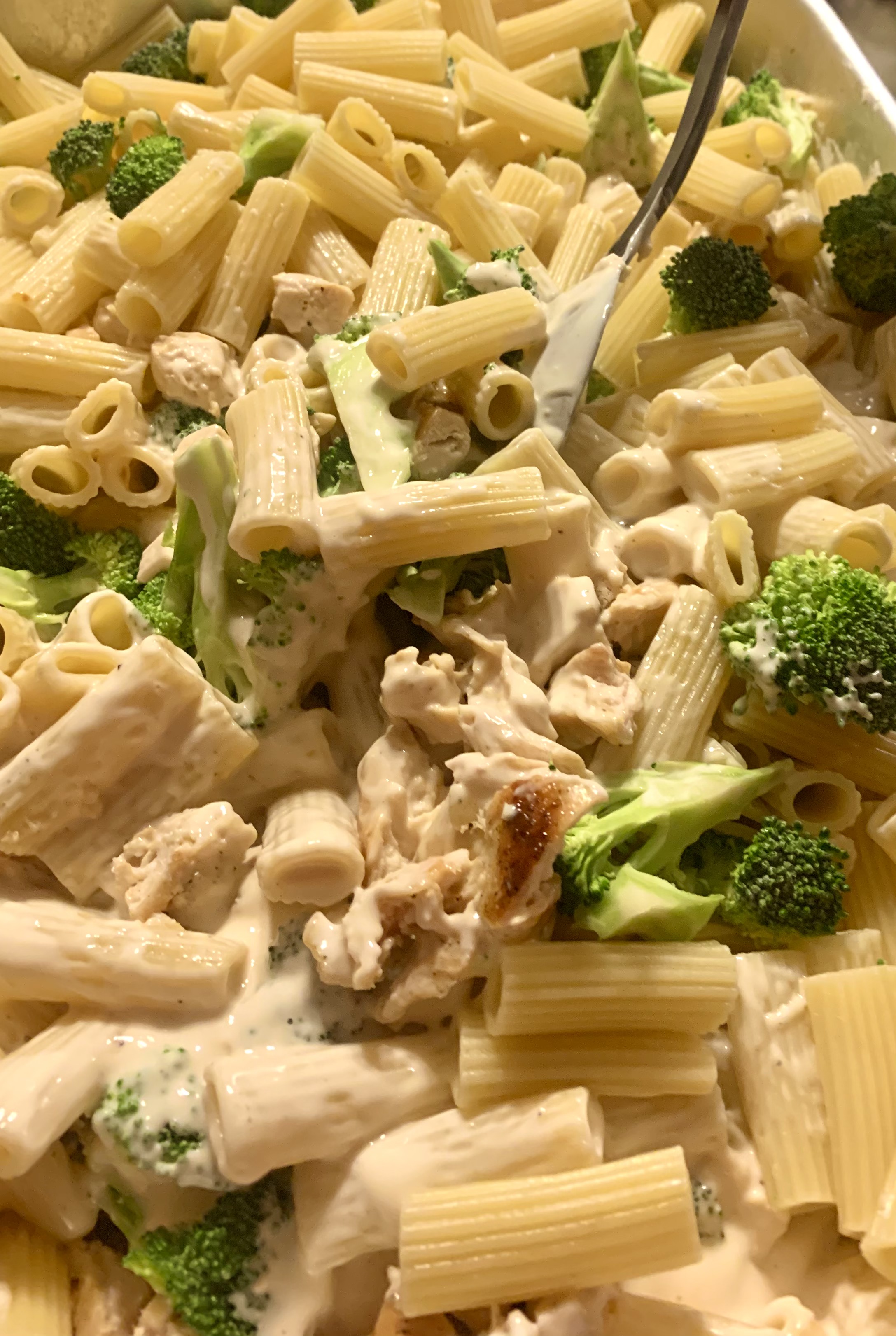 chicken broccoli and ziti being mixed together in baking dish