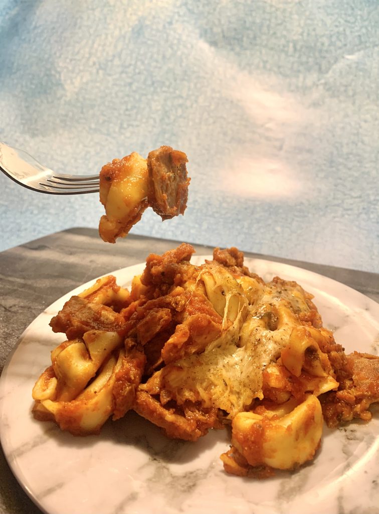 slow cooker cheesy tortellini and spicy sausage on fork