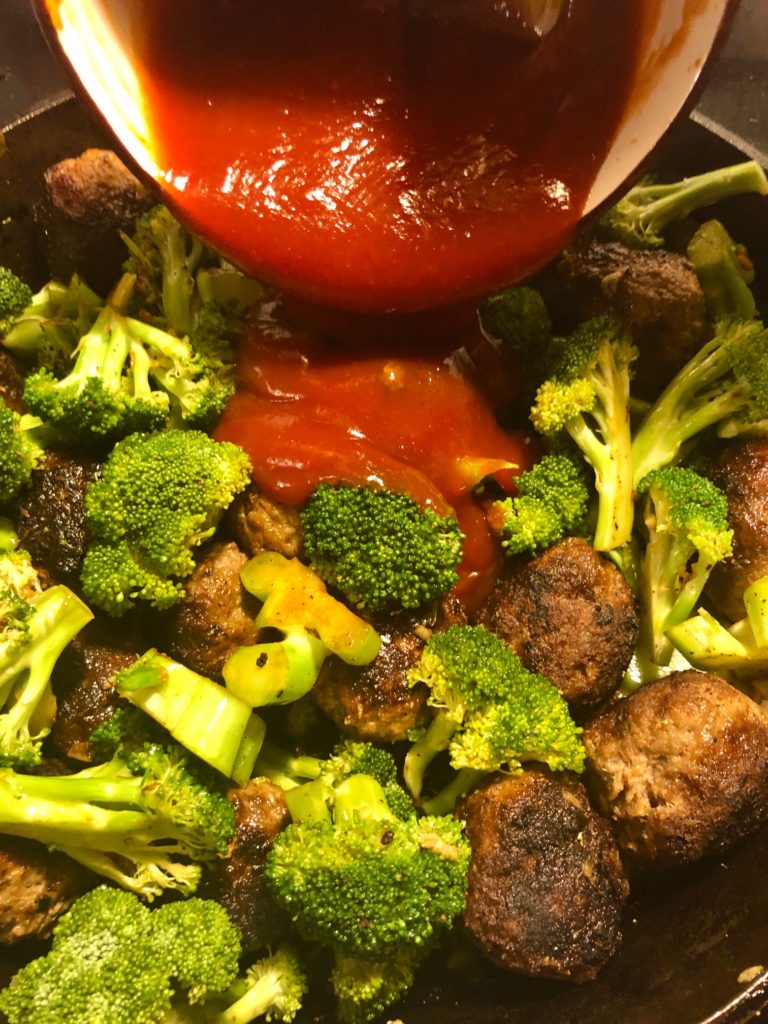broccoli and meatballs frying in skillet and gochujang, brown sugar, ketchup sauce being added