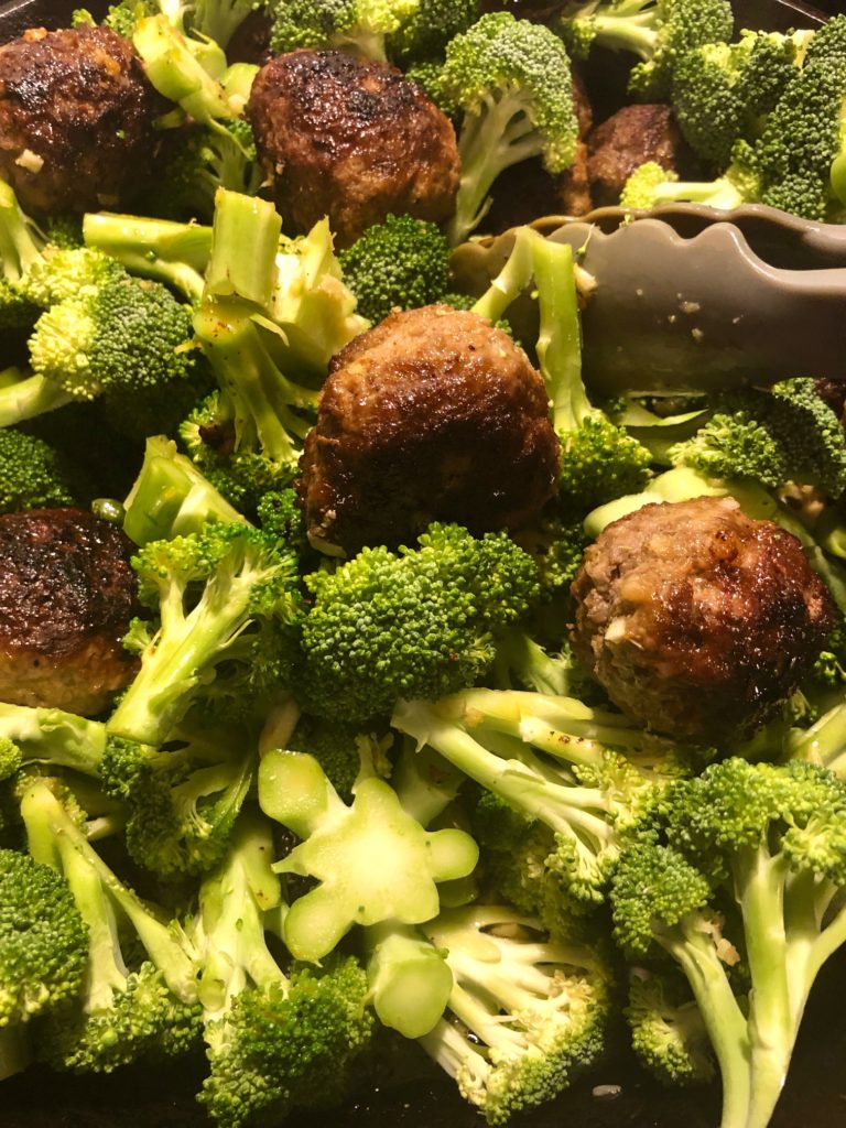 broccoli and meatballs being mixed with tongs in cast iron skillet