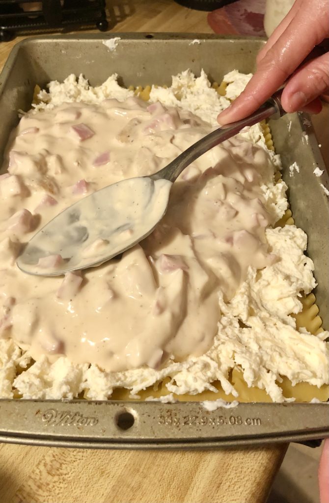adding alfredo sauce and ham to lasagna layers
