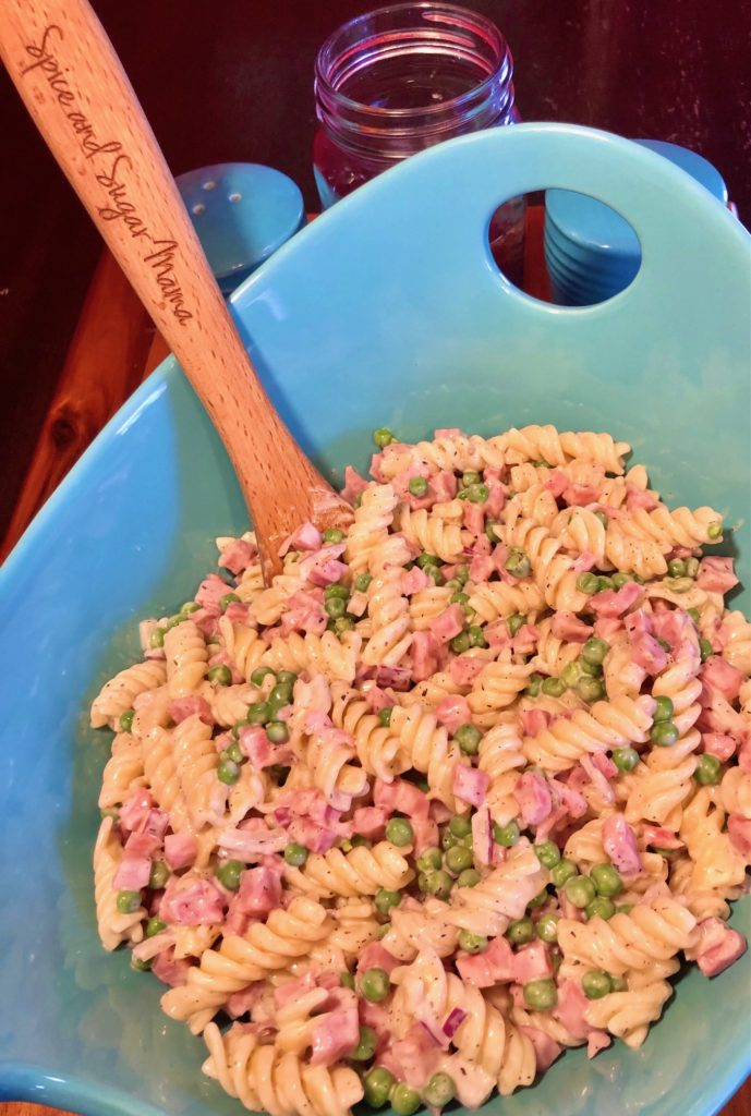 bacon ranch ham pasta salad in light blue serving bowl with wooden spoon. Rotini pasta with sweet peas, purple onion and diced ham