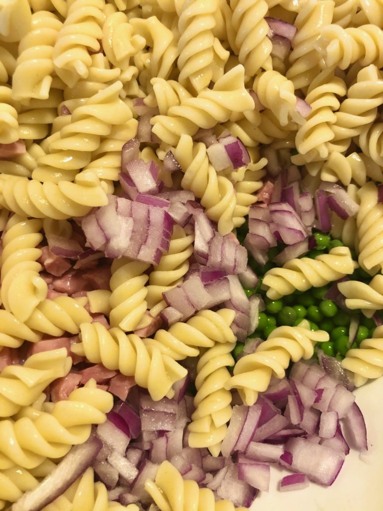 pasta salad being mixed in bowl with rotini purple onion, petite sweet peas and diced ham