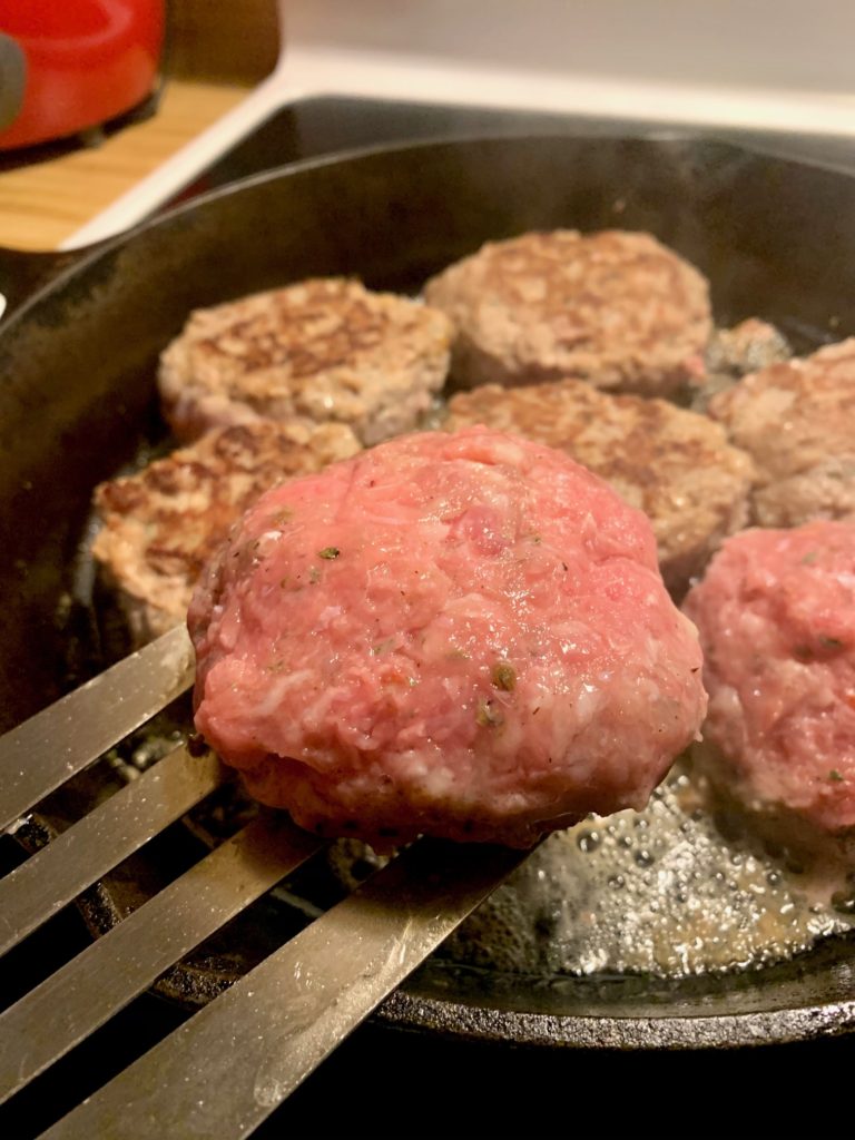 turkey sausage burgers being fried in black skillet.