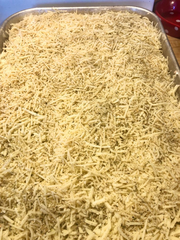 Mozzarella and parmesan cheese with black pepper and oregano covering lasagna in silver baking pan