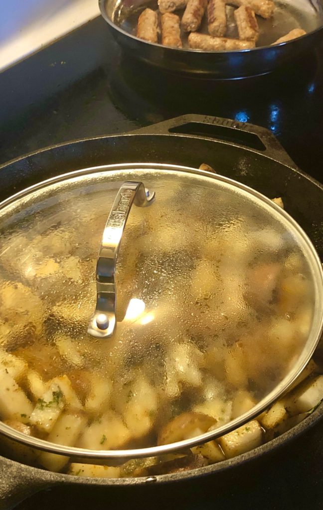 seasoned skillet breakfast potatoes frying with lid on the cast iron skillet