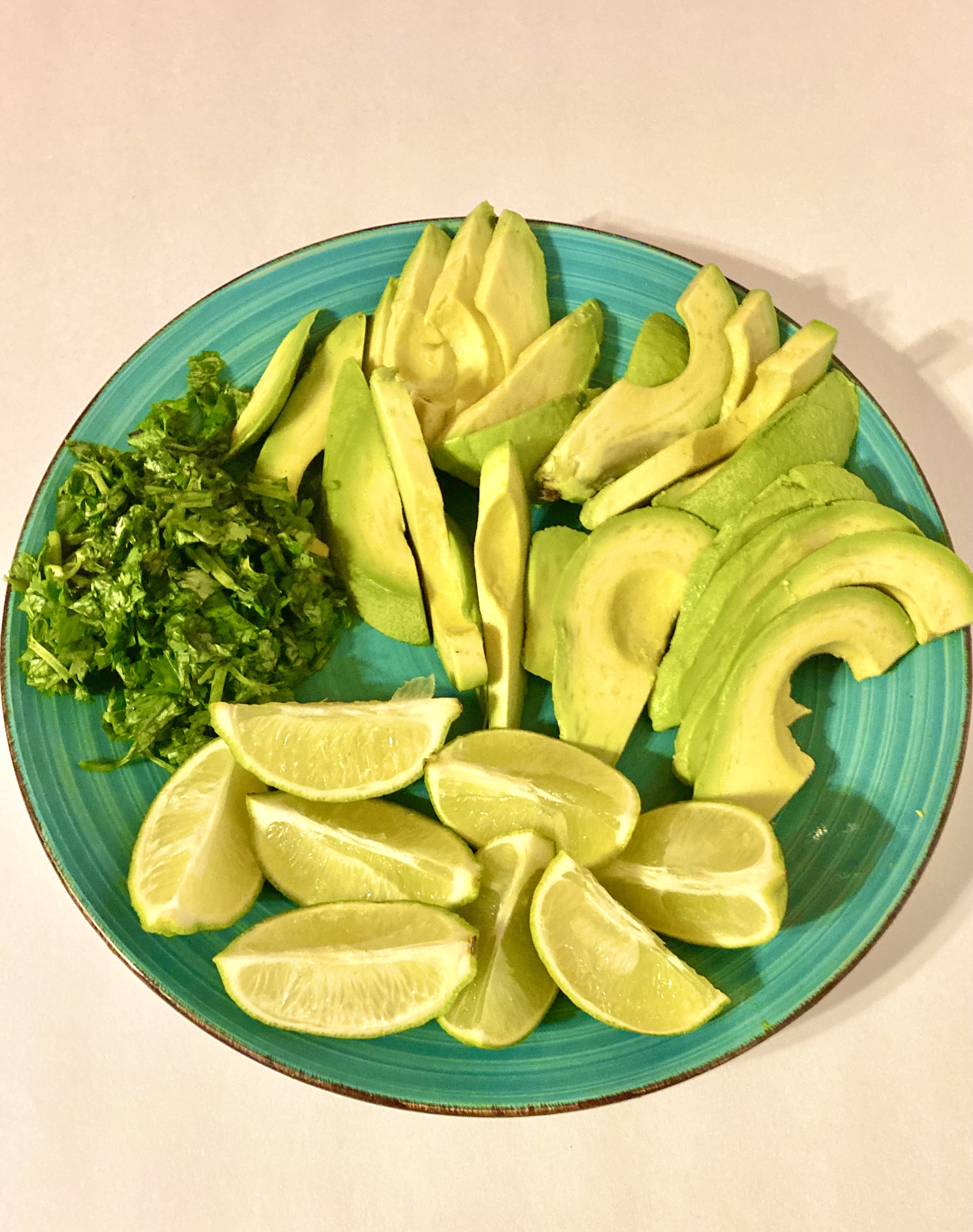 fresh cilantro with slices of lime and avocado on bright blue plate
