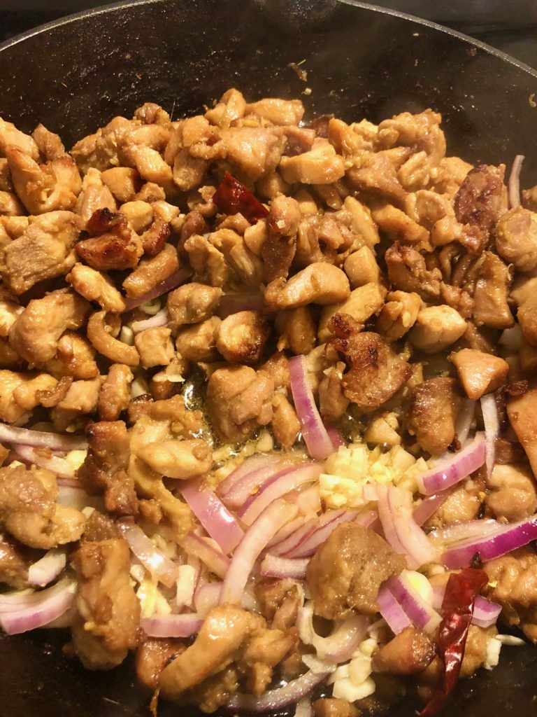 lemongrass soy sauce marinated boneless skinless chicken frying with garlic and purple onion in cast iron skillet
