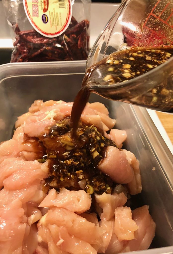 soy sauce lemongrass marinade being poured over sliced boneless skinless chicken to marinate