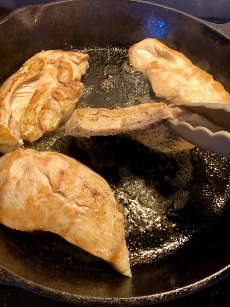 chicken tenderloins frying in cast iron skillet