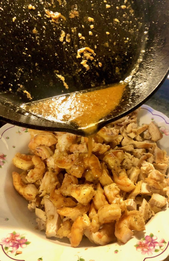 sliced chicken tenderloins and shrimp with sauce being poured over the bowl from cast iron skillet overhead