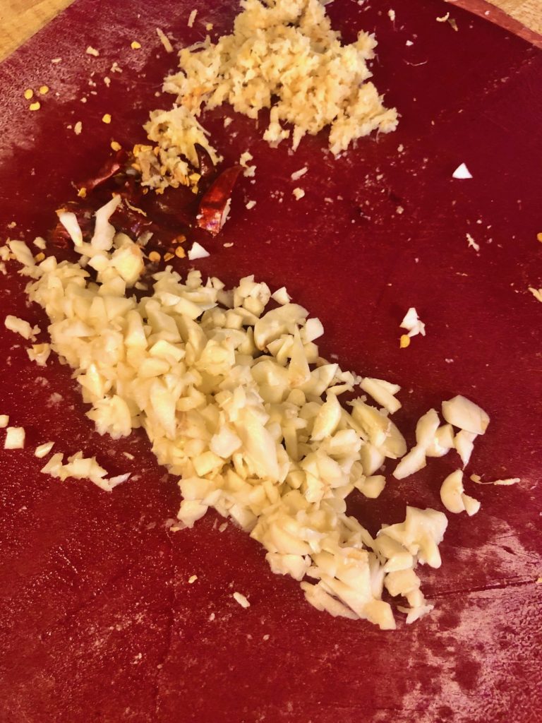 garlic ginger and thai chilis on chopped on red cutting board