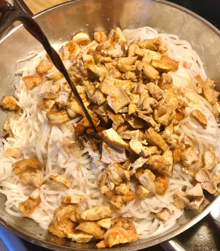 adding pad thai sauce to pan with shrimp, chicken and rice noodles