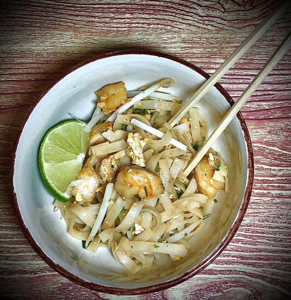 pad thai plated with chopsticks and served with lime wedge. rice noodles, scrambled eggs, bean sprouts, shrimp and chicken.
