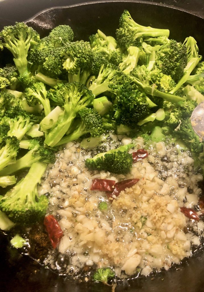 garlic ginger thai chilis and broccoli frying in cast iron skillet