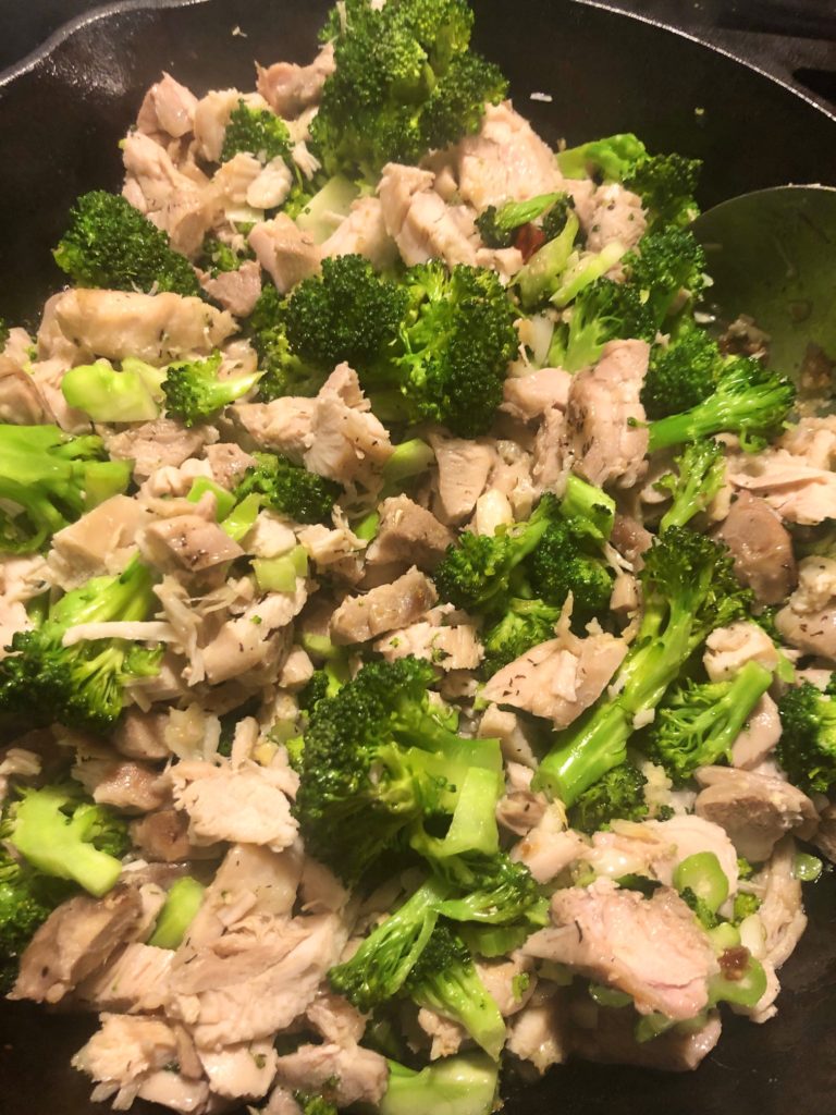 mixing broccoli and boneless skinless chicken breast in cast iron skillet