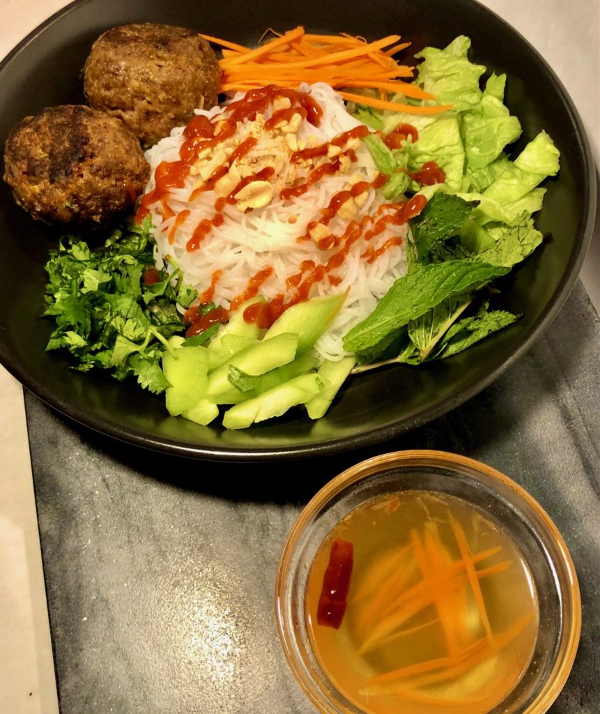 vietnamese bun bowl with thai meatballs on black plate. meatballs are on a bed of lettuce, bean sprouts, rice vermicelli, cucumber, carrots, mint, cilantro, sriracha and chopped peanuts