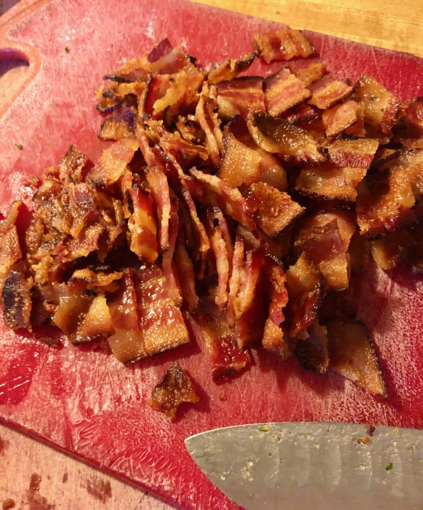 chopped crisp bacon on red cutting board lying beside knife