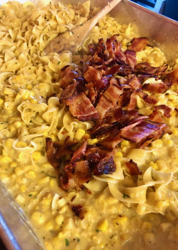 egg noodles with corn chowder and topped with crisp bacon in silver casserole dish