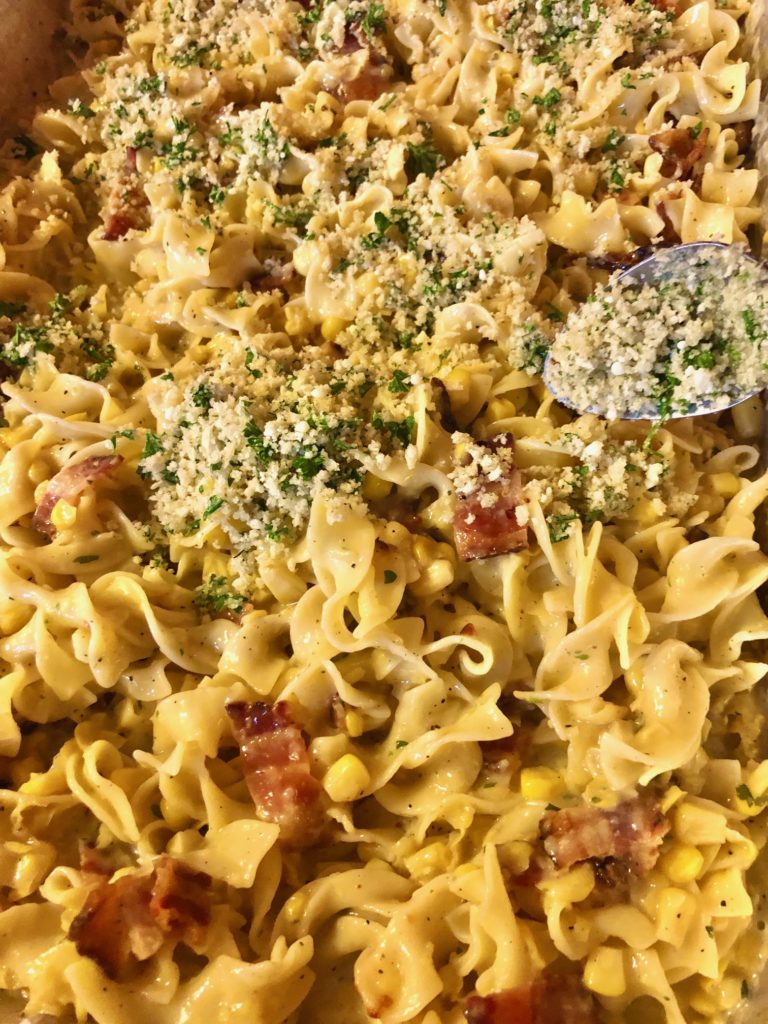 corn chowder casserole with bacon being topped with a parmesan cheese, fresh parsley and panko breadcrumb topping