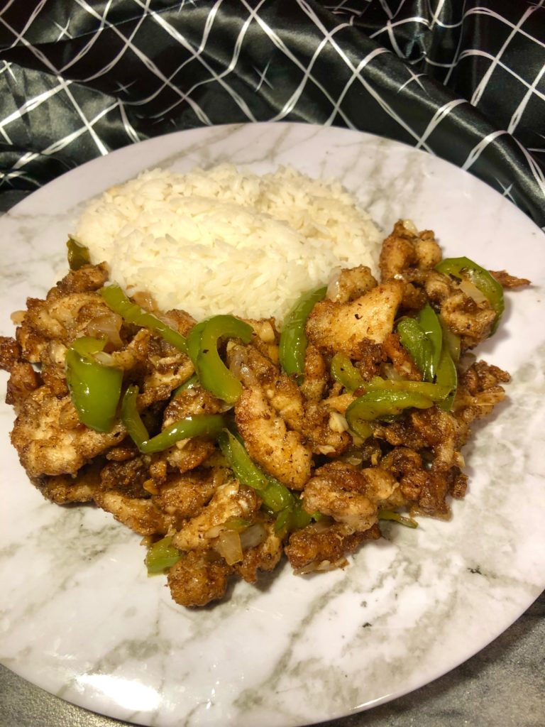 Chinese pepper chicken served with jasmine rice. plated on white and gray marble plate with dark gray marbled cutting board and black and white napkin in the background