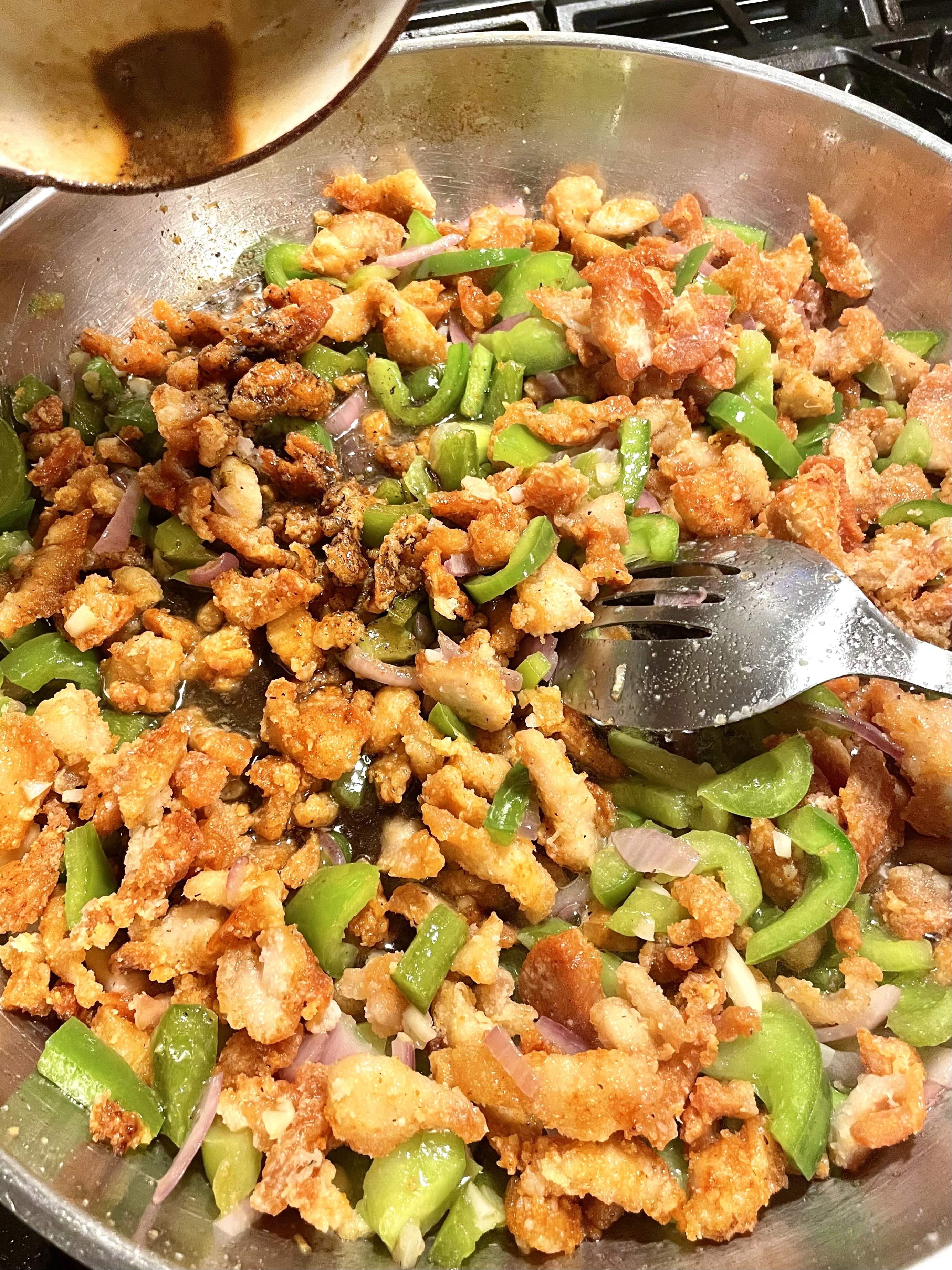 Chinese pepper chicken with sauce being added in the pan.