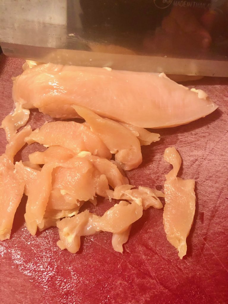 slicing chicken breast with butcher knife on red cutting board