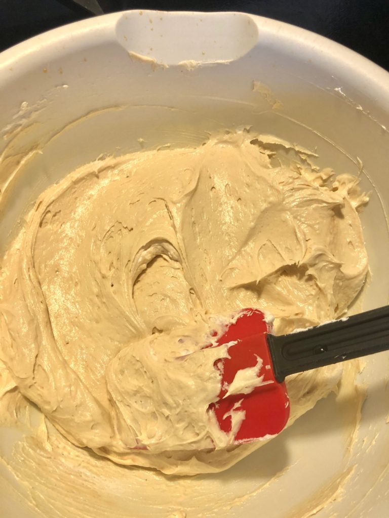 peanut butter frosting in white mixing bowl with red rubber spatula