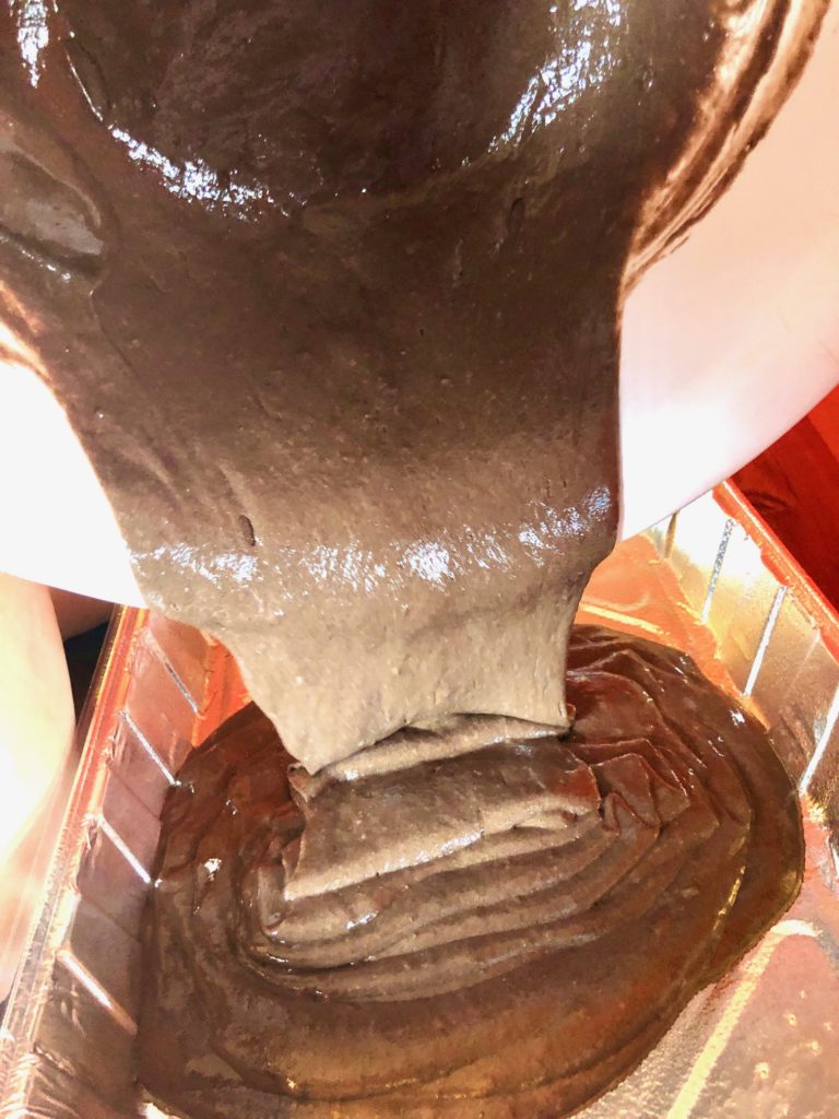 pouring prepared cake batter into foil pan from white mixing bowl